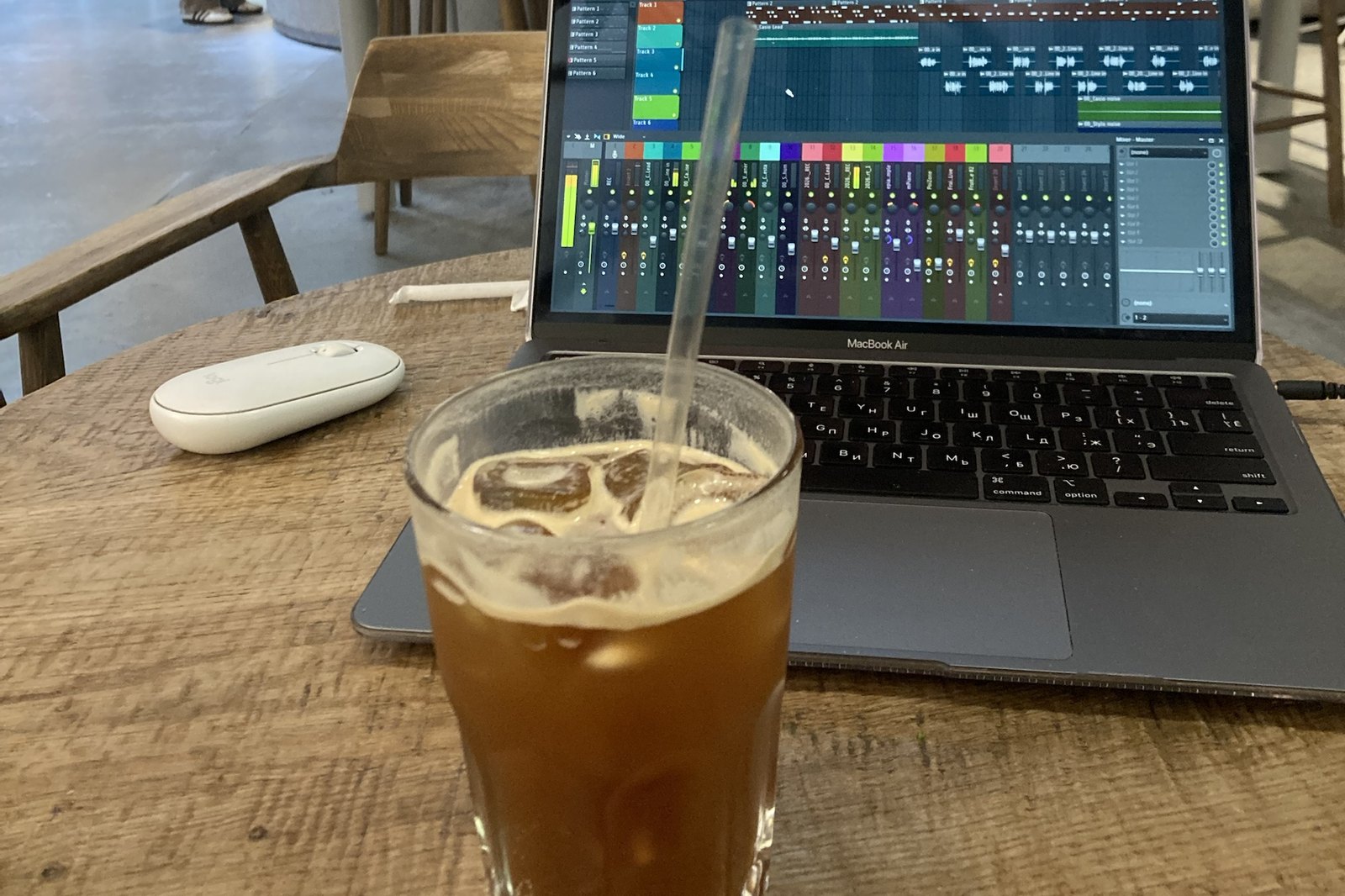 MacBook с открытым микшером FL Studio на столе в кафе, рядом стакан кофе — баланс собирается где угодно
